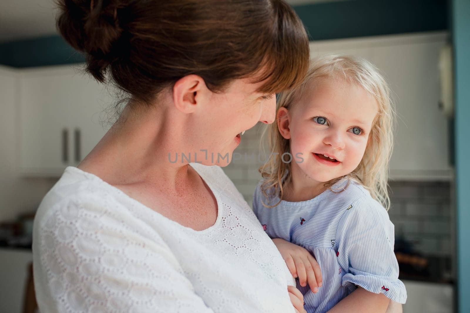 Side view of a mother talking and smiling at her daughter who is also smiling. The mid adult mother is holding her daugher and caring for her.