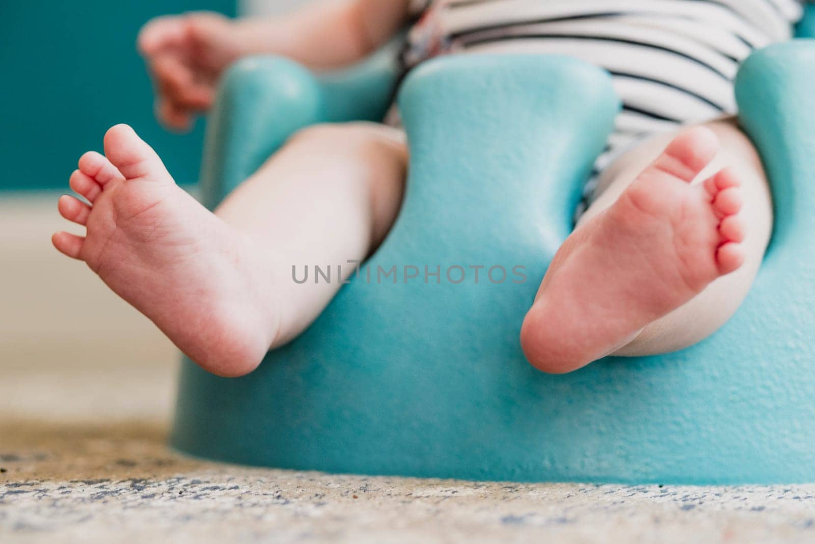 Low angle front view of a unrecognisable baby. The baby is sitting in a floor seat, the focus is on the babies feet.