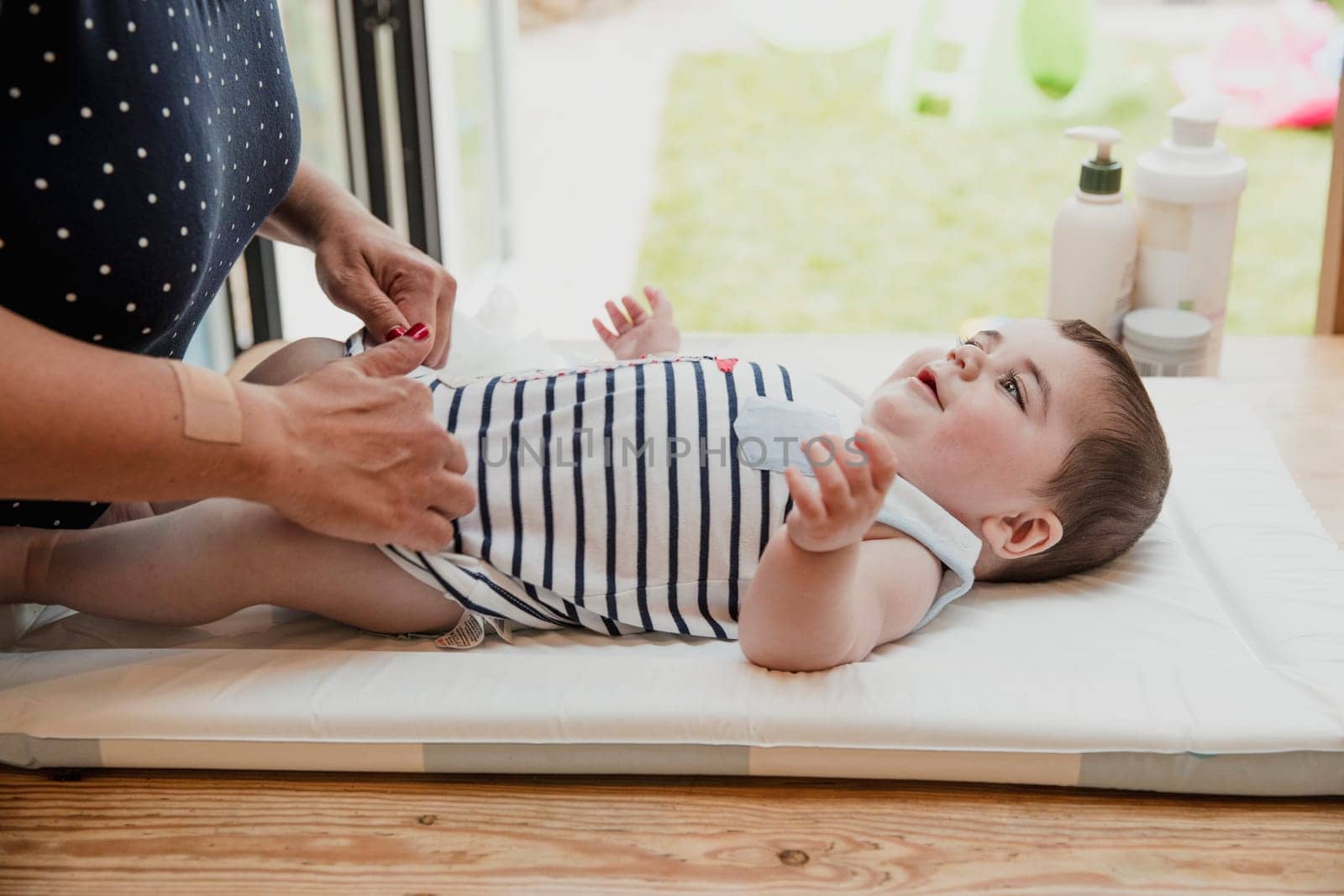 Side view of a baby boy lying on his back. The little boy is getting his nappy changed by his mother who is unrecognisable.