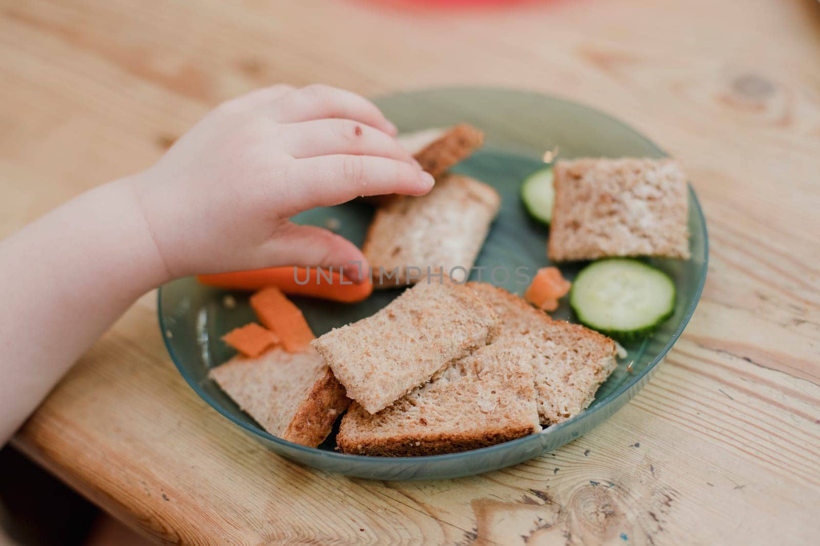 Point of view angle of a little girls hand reaching to pick some food off her plate. She is having a healthy snack.