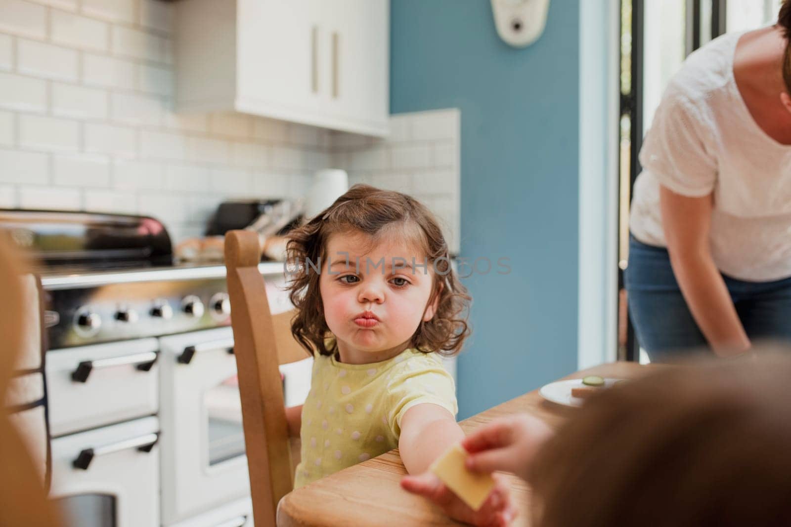 Point of view angle of a little girl being handed some food at the kitchen table. The little girl is focused on the food and has crumbs around her mouth.