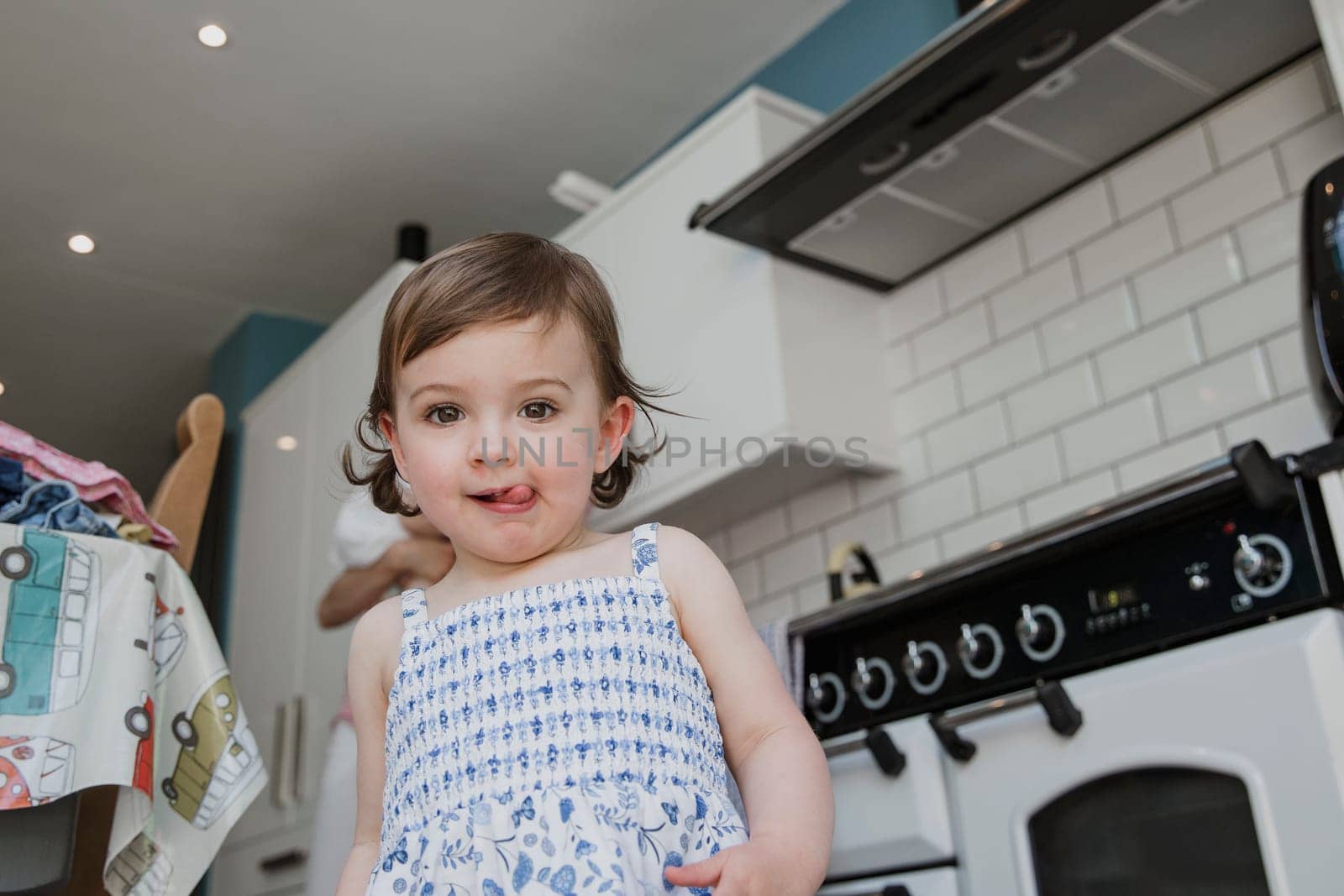 Low nagle view of a little girl looking at the camera. She is stood in the kitchen and pulling a cheeky facial expression with her tongue sticking out.