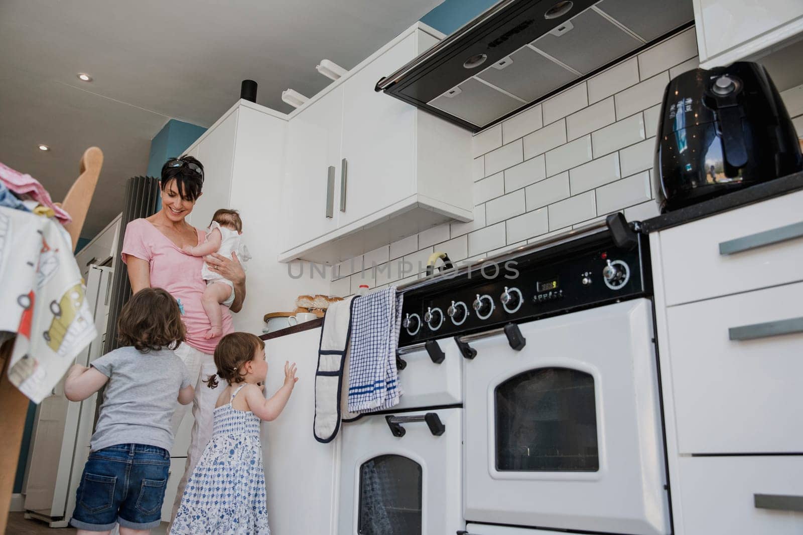 Low angle view of a mother with her three daughters standing in the kitchen. Two of the little girls are stood trying to get the attention of their mother.