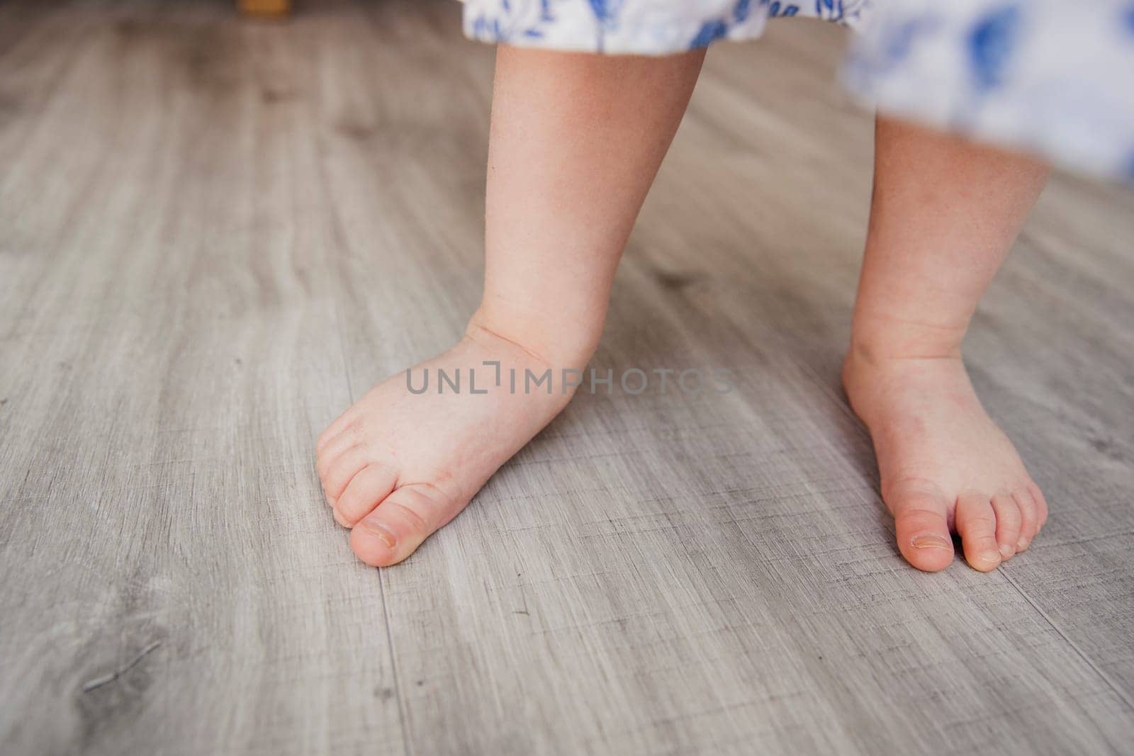 Low angle view of a little girls bare feet on a hard wood floor. The little girls face is unrecognisable.