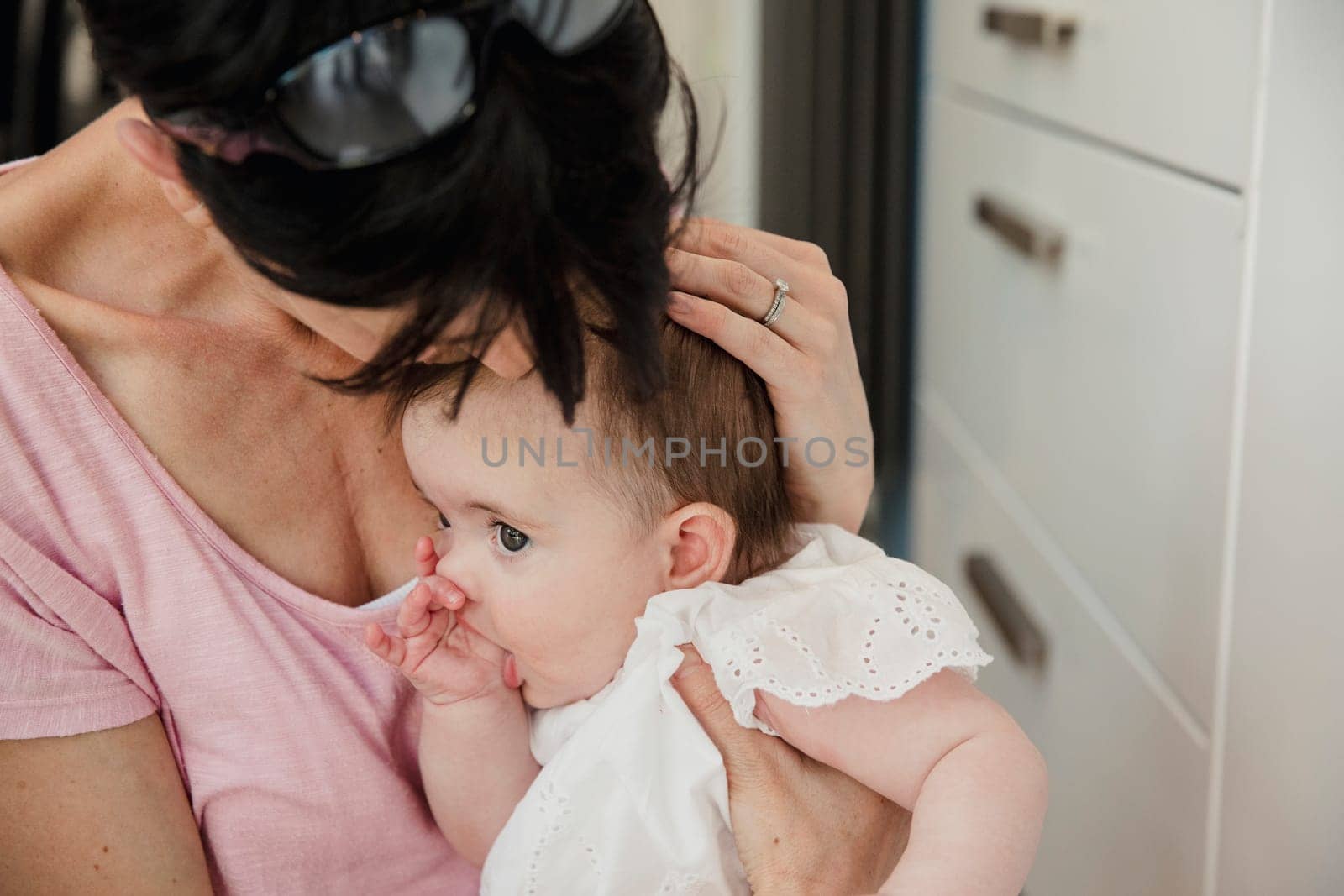 Close-up of a mid adult mother holding her baby daughter close and comforting her as she sucks her thumb. They are wearing casual clothing an sitting down