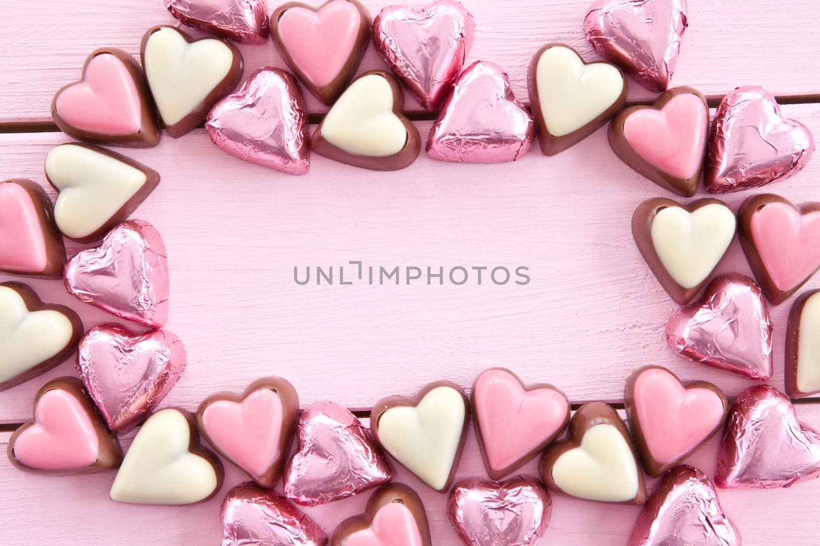 Colorful chocolates in heart shape on pink background made of wood