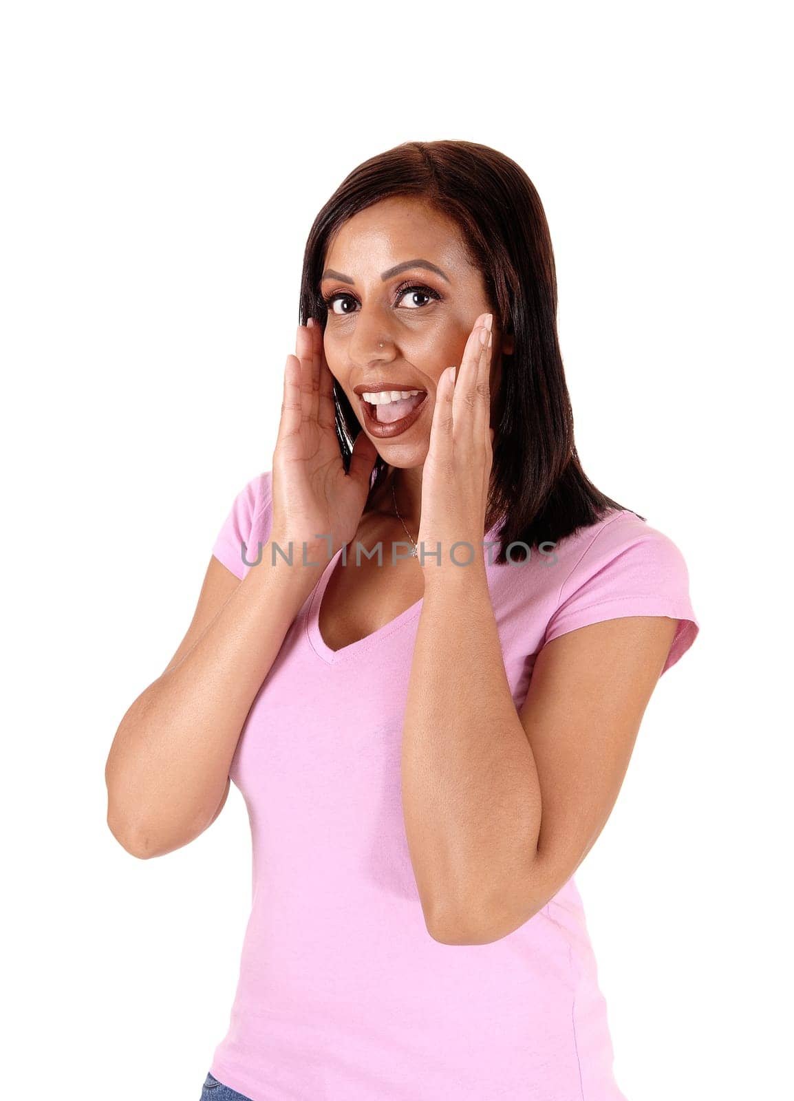 A surprised young woman standing with her hands on her face an.and open mouth, in pink shirt, isolated for white background.