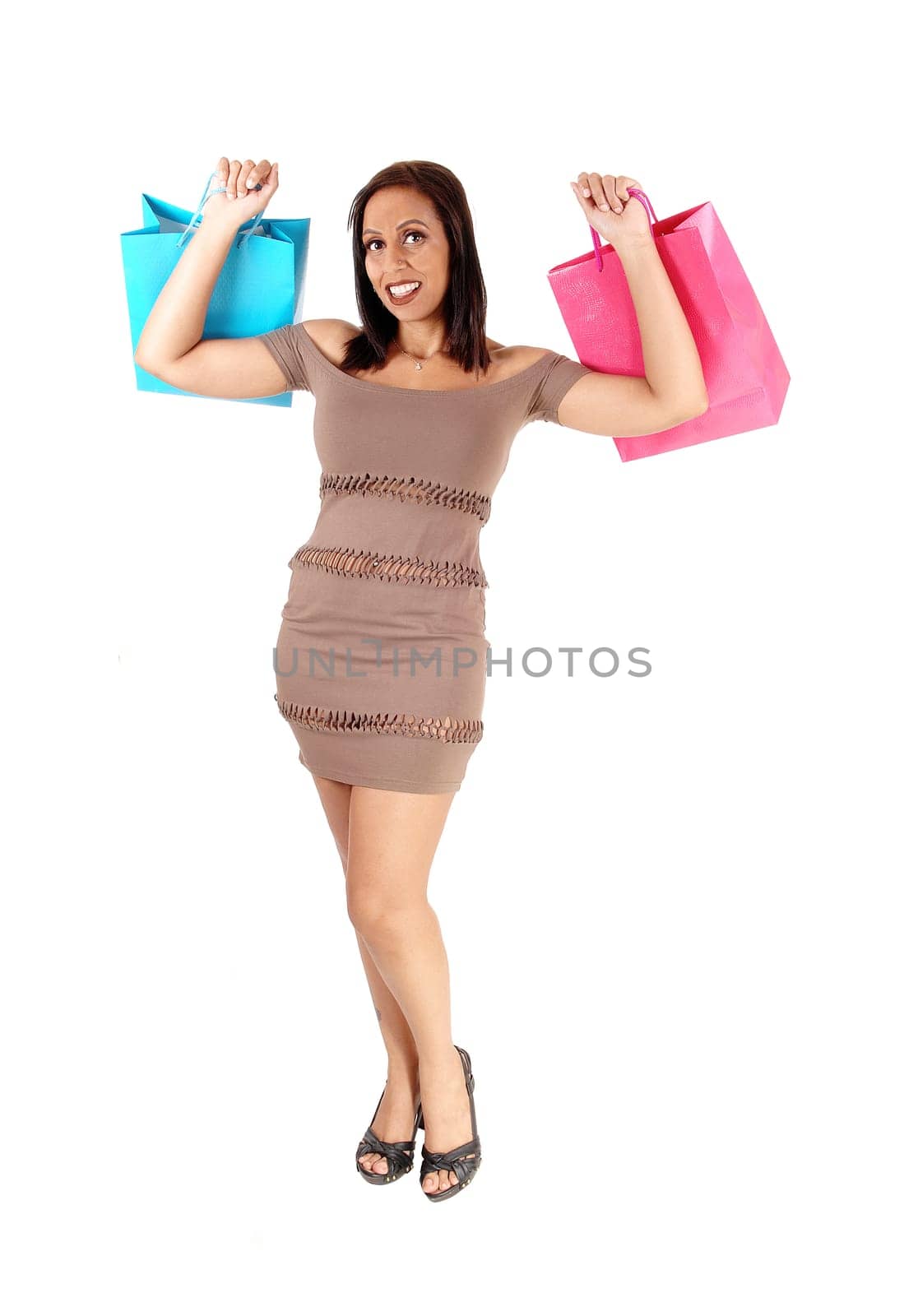 A lovely young woman standing in a brown dress and heels holding up.her shopping bags is happy, isolated for white background.