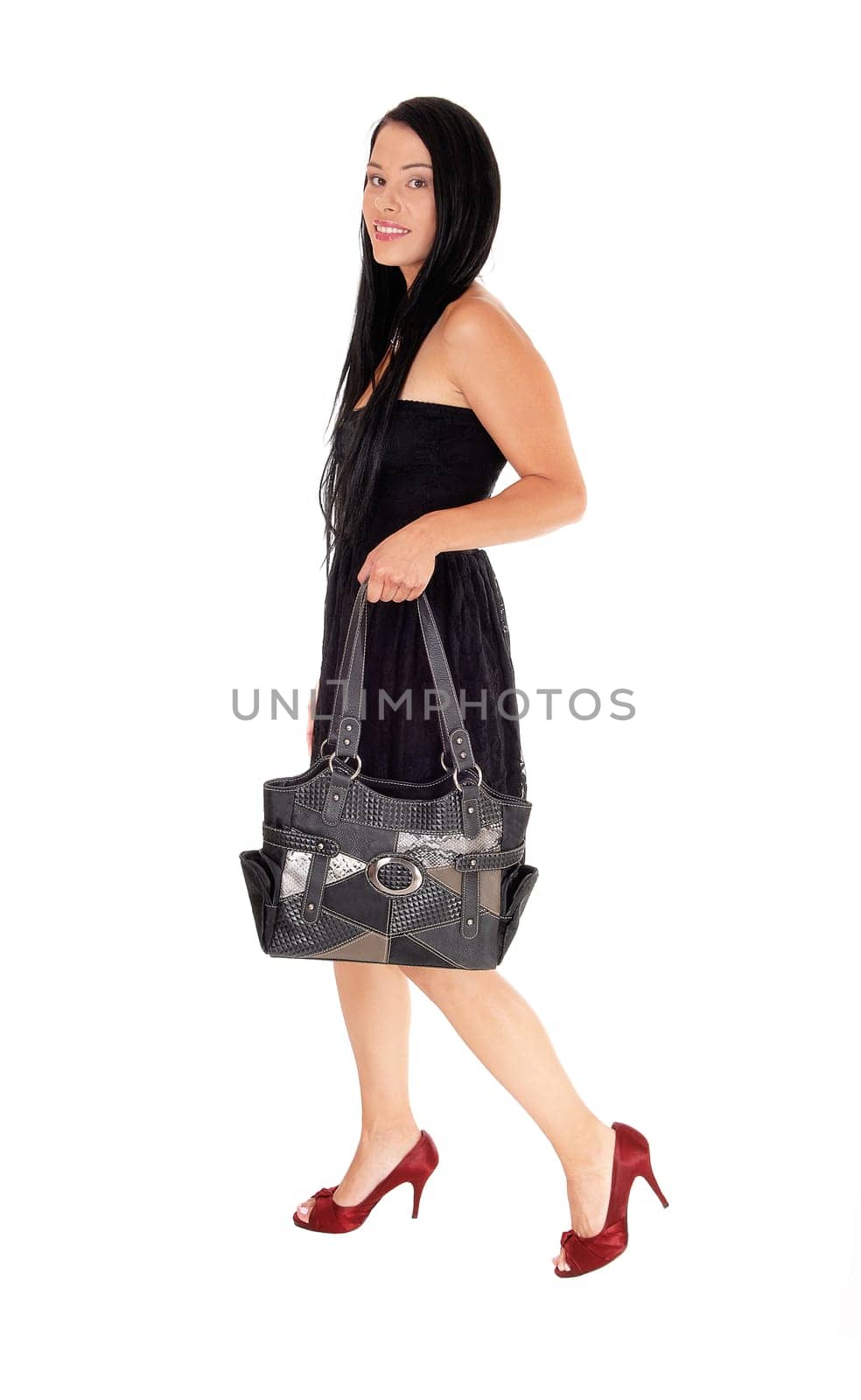 A beautiful woman walking in a black dress holding her handbag.and in red heels and long black hair, isolated for white background.