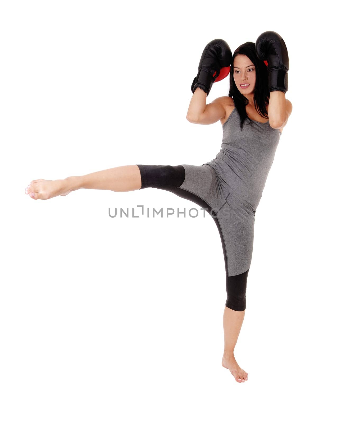 A slim young woman in exercising outfit praxis kick boxing with her.black cloves, standing on one leg, isolated for white background.