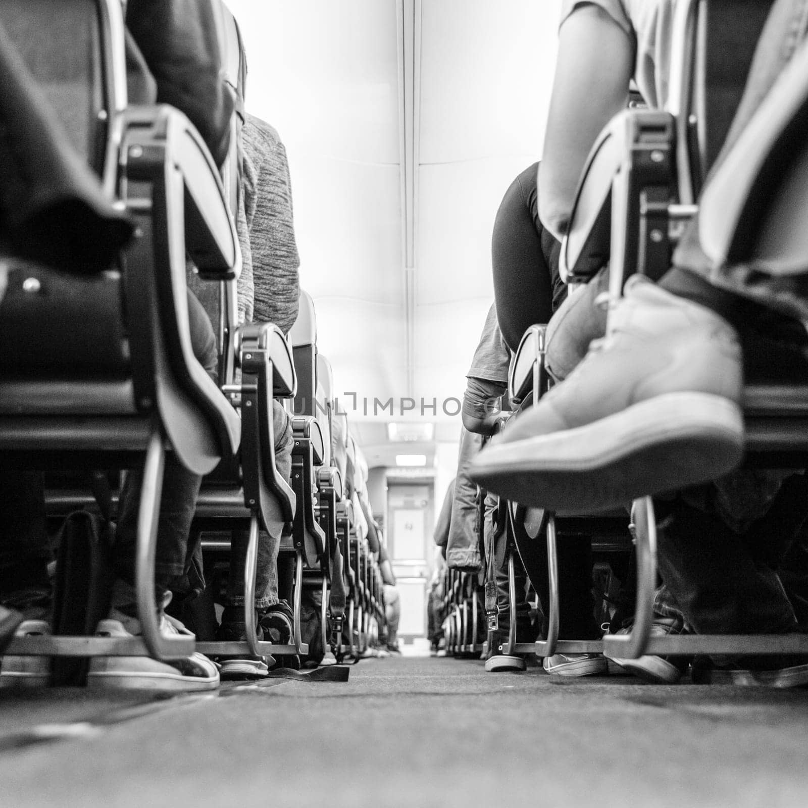 Low agle view of passenegers commercial airplane aisle with passenegers sitting on their seats while flying. Black and white image.