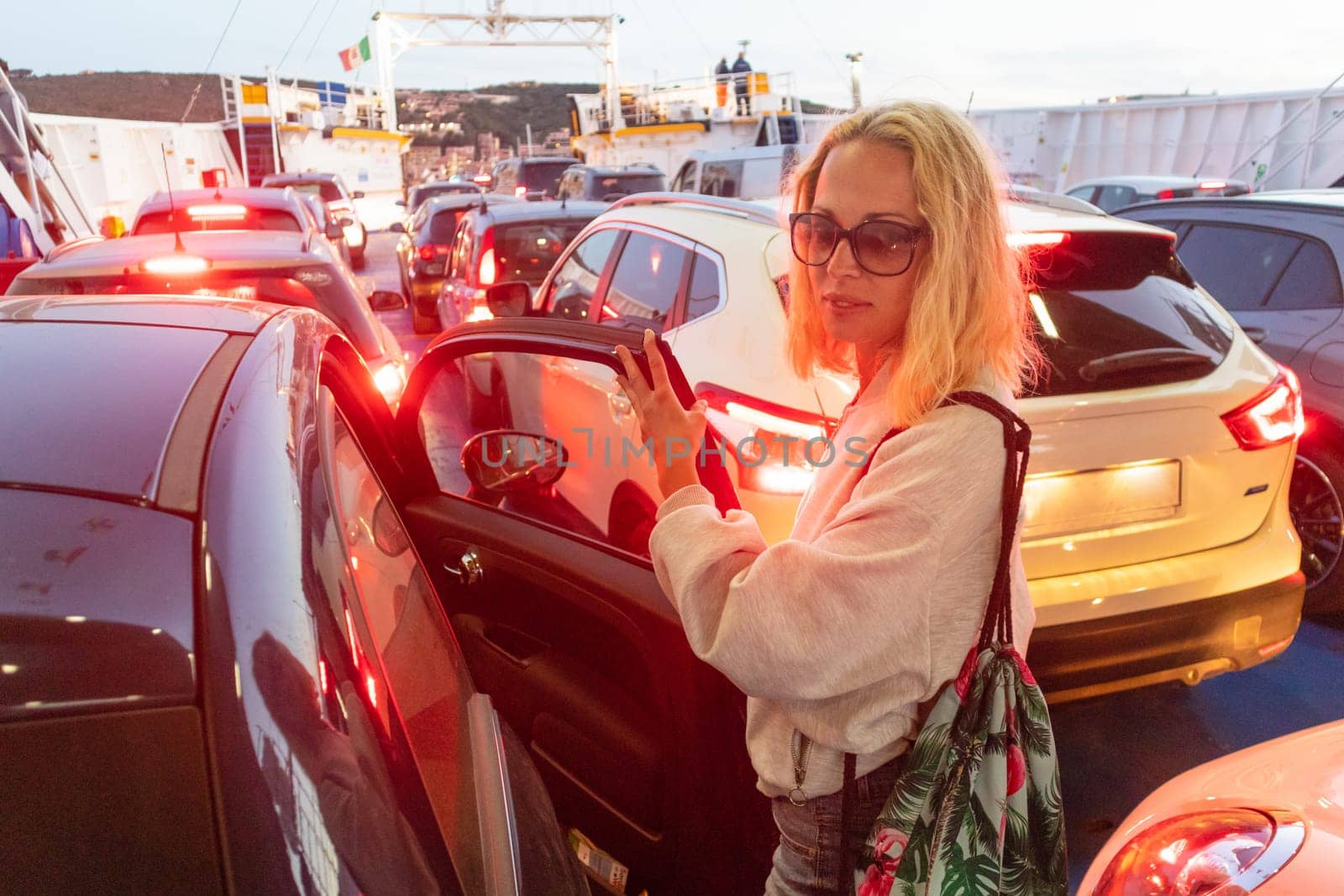 Woman on ferry boat trip to their summer vacations island destination. Sardinia, Italy at dusk. Lady entering the car before vehicle disembarkment.
