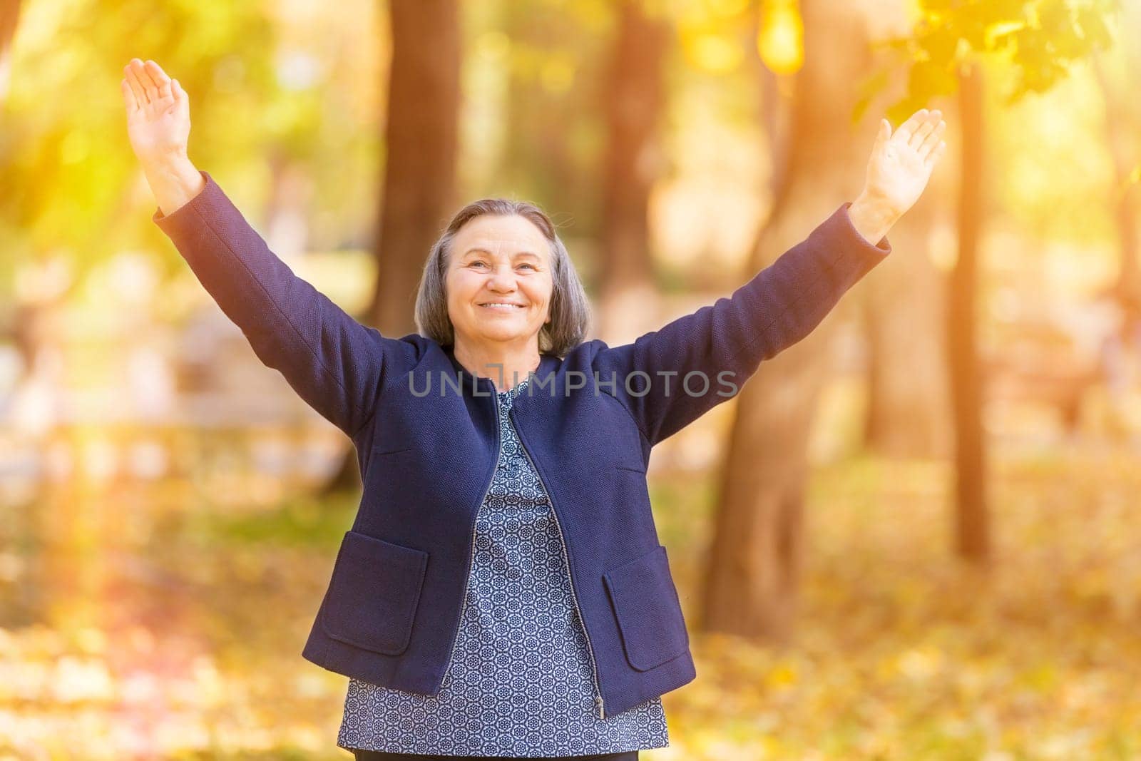 Casual senior woman with arms outstretched standing in autumn park.
