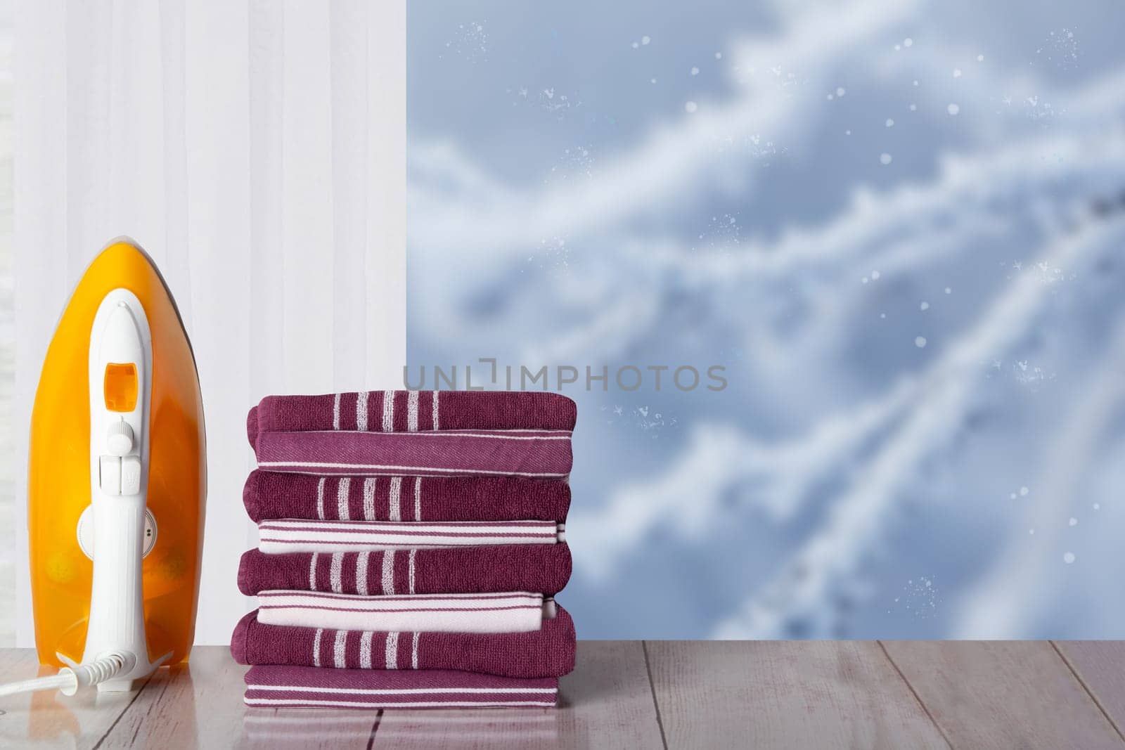 Closeup of yellow iron and a stack striped towels on rustic table in front of window with blurred winter landscape. Template for your display product montage. Space.