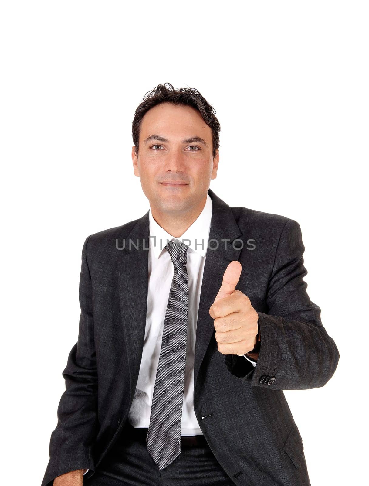 A young business man sitting in a dark gray suit and tie showing his.approval with his thump up, isolated for white background.