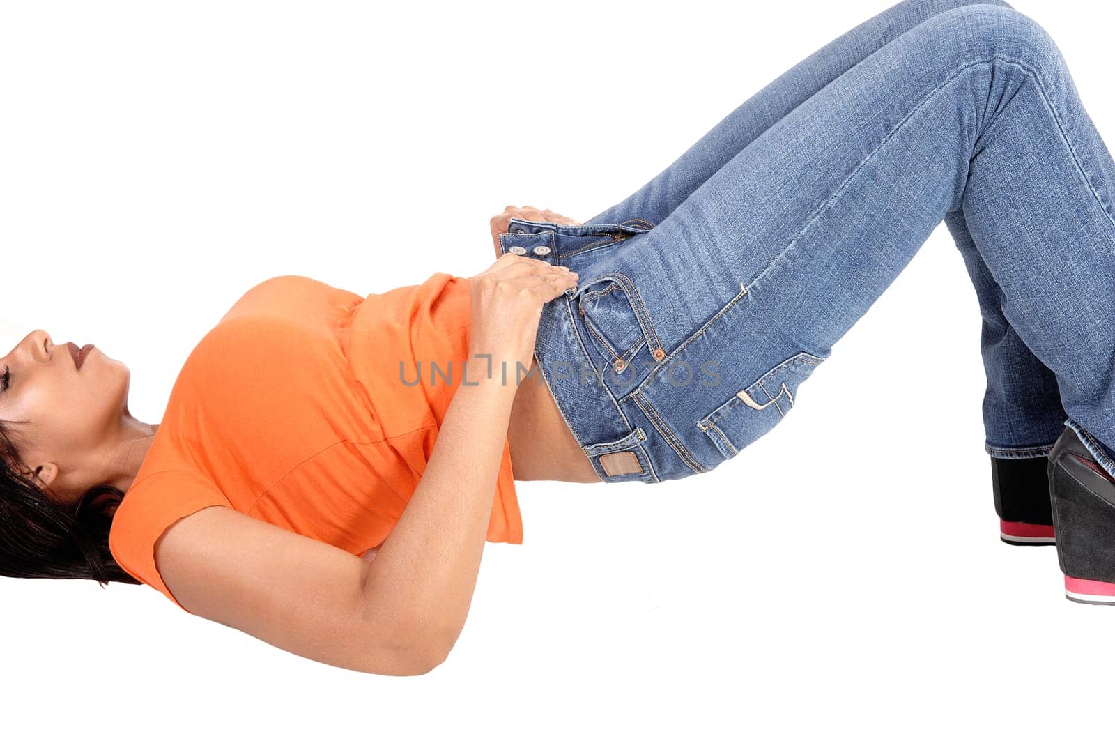 A slim young woman lying on her back on the floor try to put her jeans.on, lifting her butt, isolated for white background.