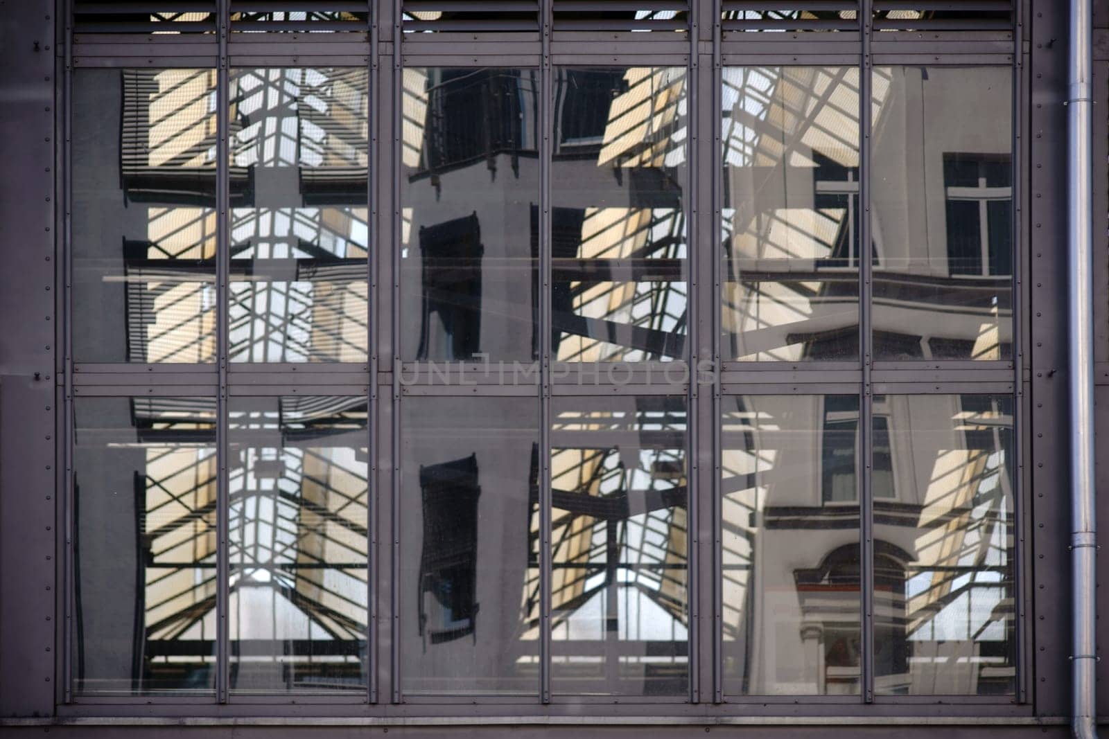 The detail of a steel construction with windows and a reflecting metal roof construction behind it.