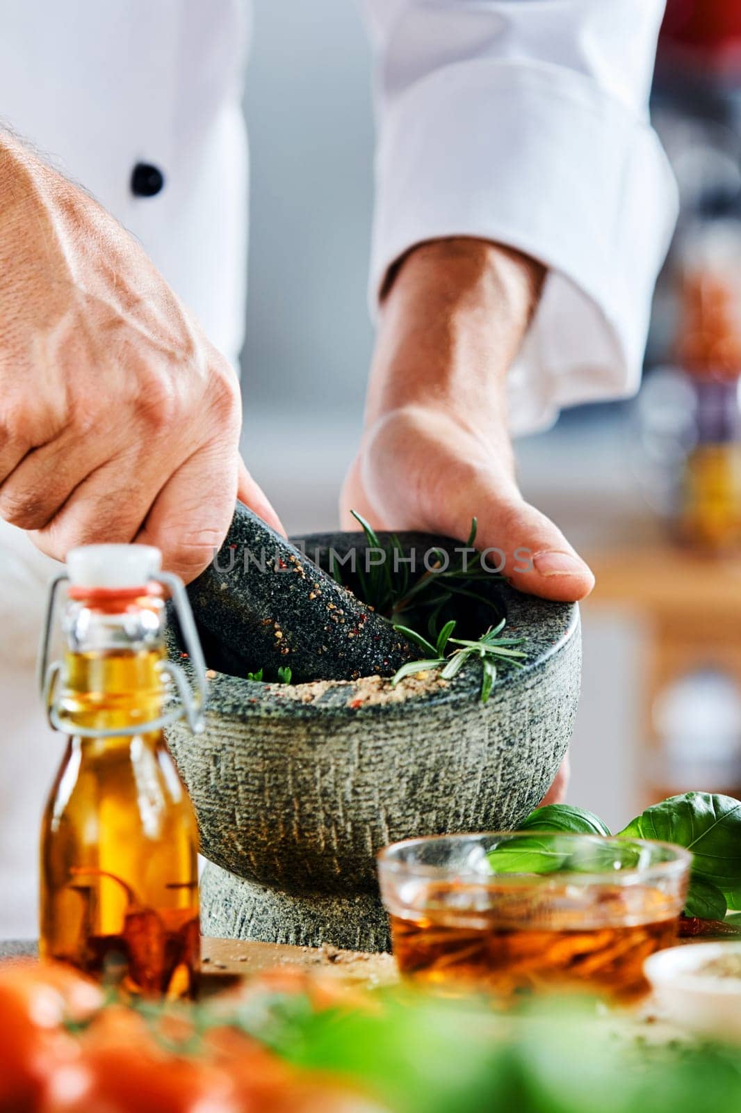 Chef grinding fresh herbs and spices in a pestle and mortar with a freshly prepared marinade and fresh ingredients for a salad