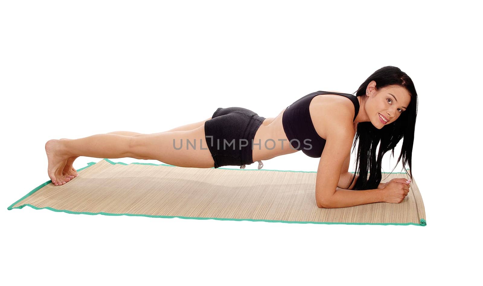 A pretty young woman lying on her stomach in black sports outfit doing.push up's, looking into camera, isolated for white background.