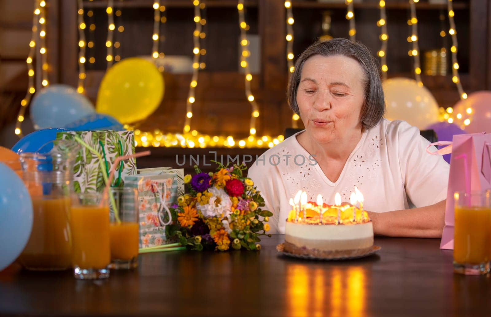 Elderly woman celebrating her anniversary at home. Senior woman blowing candles on birthday cake. Celebrating aging concept.