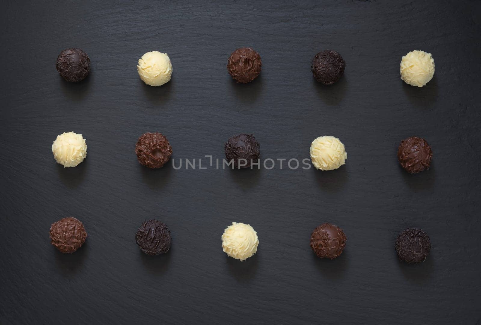 Fancy dark milk white chocolate truffles ready to eat on black stone background.