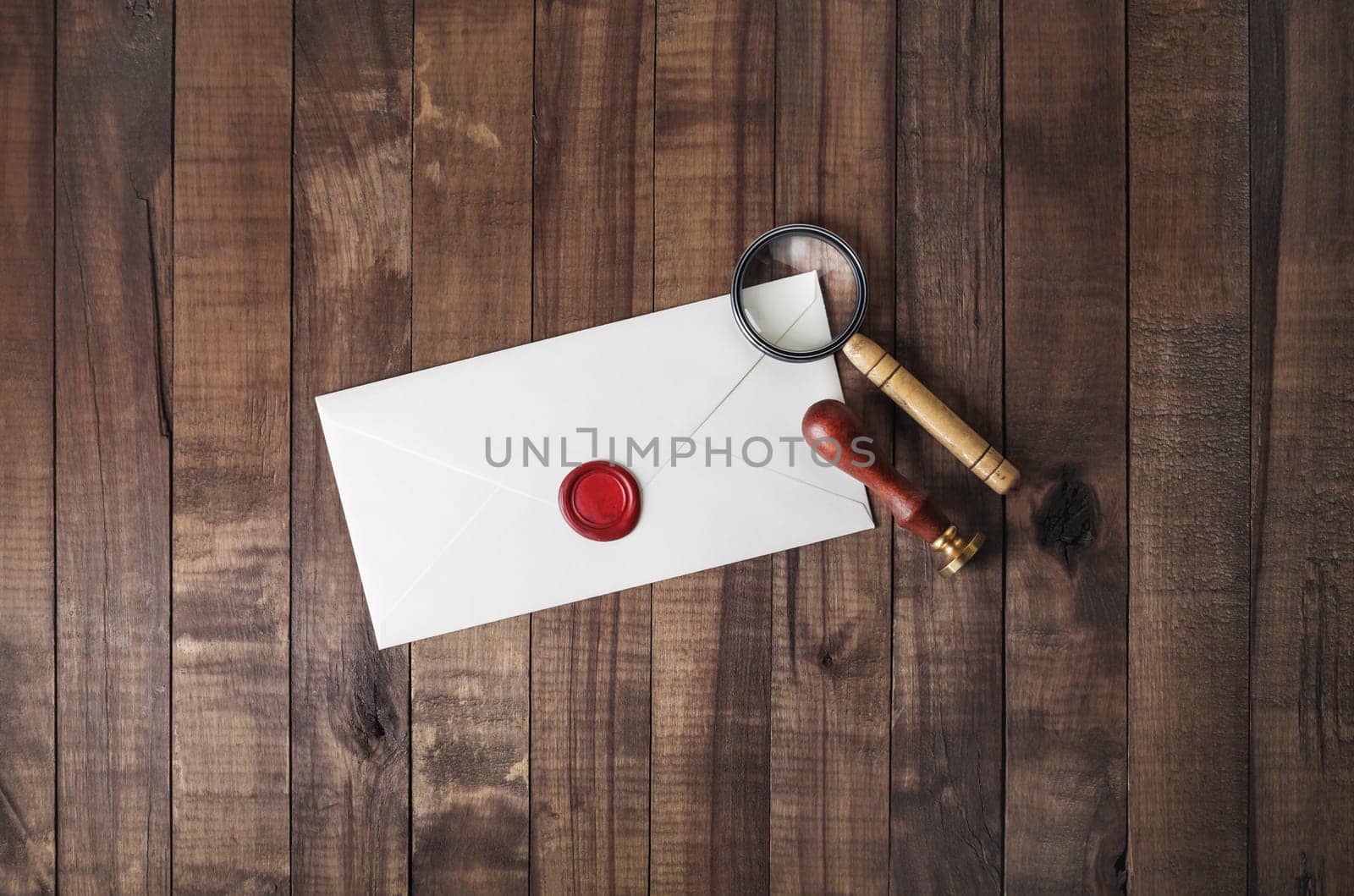 Blank paper envelope with wax seal, stamp and magnifier on wood table background. Mockup for your design. Flat lay.