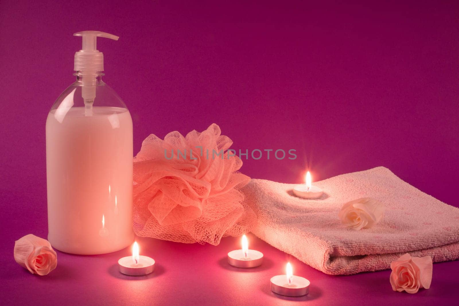 Shower gel, bath sponge, towel with some flowers and candles are on pink background. Shower, bath, wellness and spa.