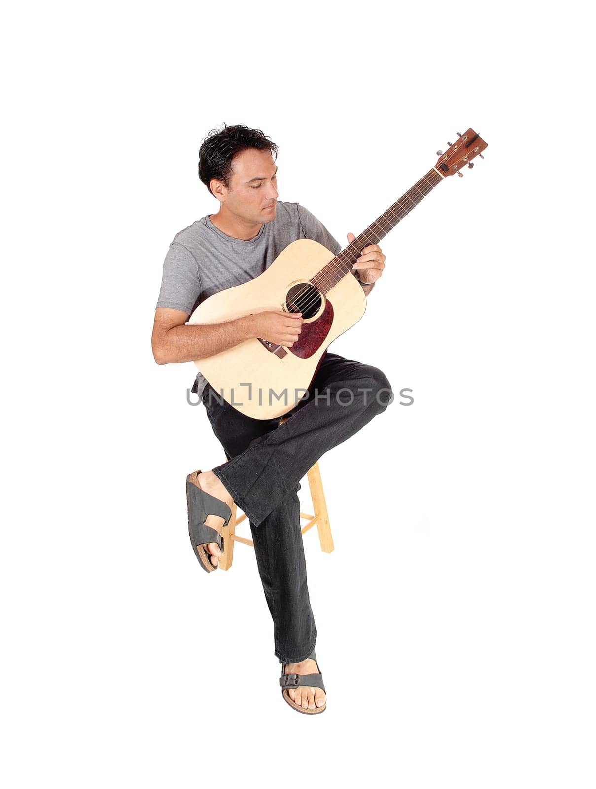 A handsome young man sitting in casual clothing playing his guitar.and singing for himself, isolated for white background.