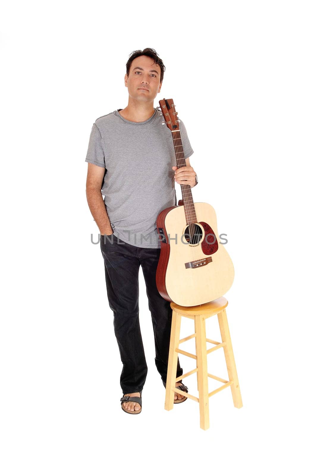 A young handsome man taking a brake from playing the guitar, standing.in jeans gray shirt, sandals, isolated for white background.
