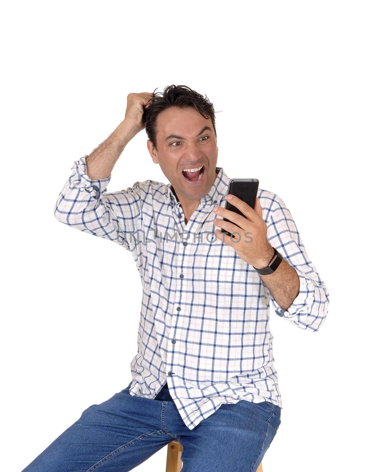 A young man holding up his phone, looking very surprised what is on his.phone, scratching his head, isolated for white background.