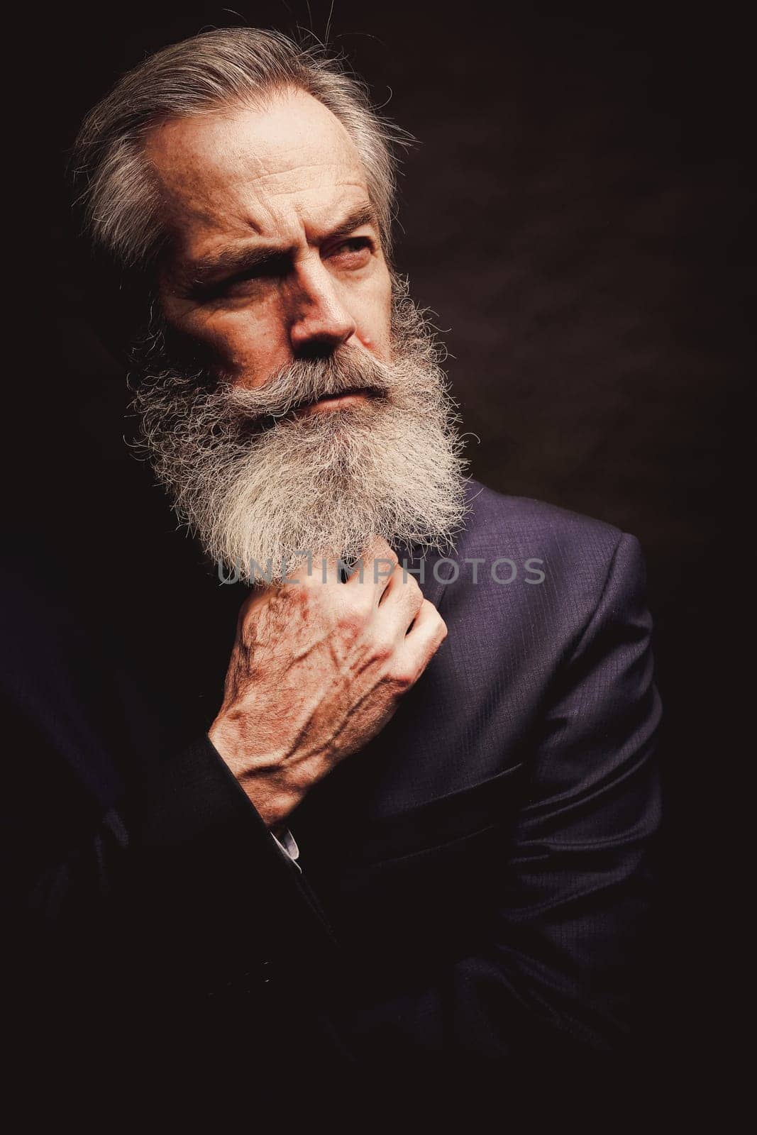 close up of senior man with grey hair and full beard, wearing suit on dark background