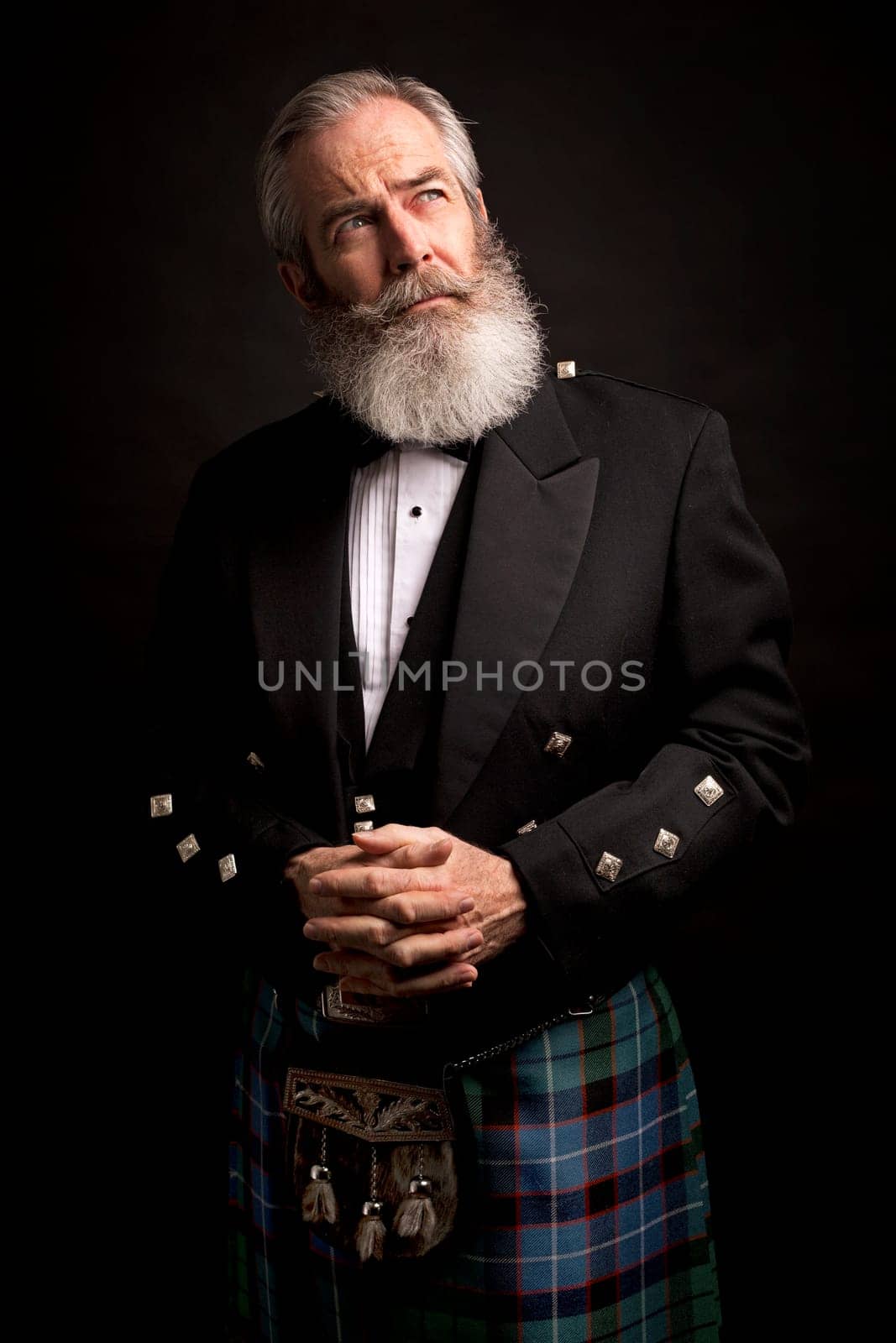 close up of senior man with grey hair and full beard, wearing scotting kilt on dark background