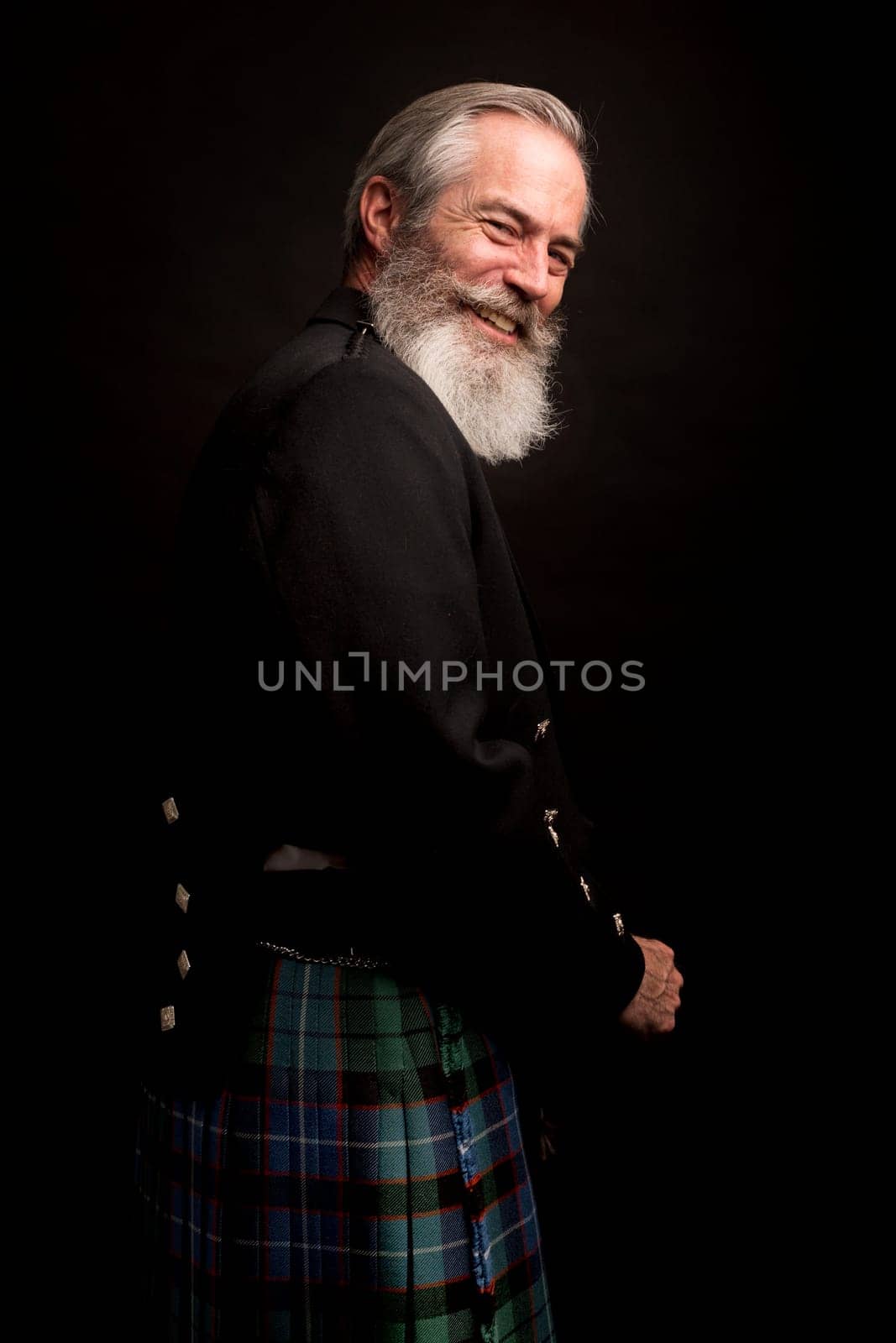 close up of senior man with grey hair and full beard, wearing scotting kilt on dark background