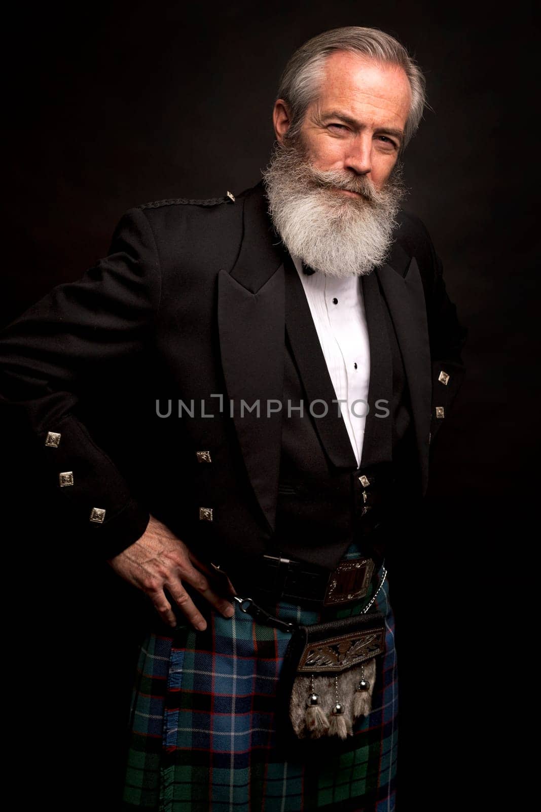 close up of senior man with grey hair and full beard, wearing scotting kilt on dark background