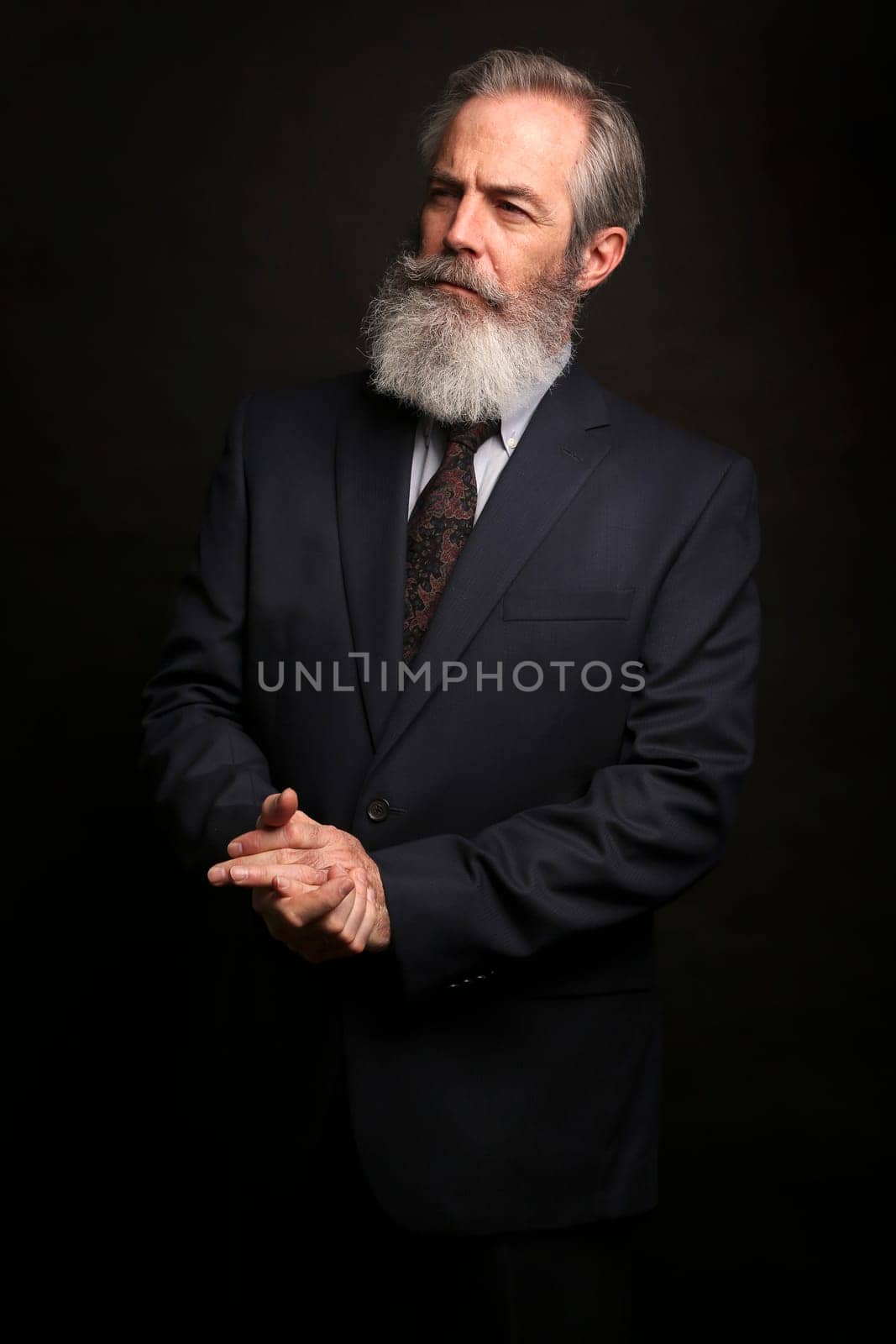 close up of senior man with grey hair and full beard, wearing suit on dark background
