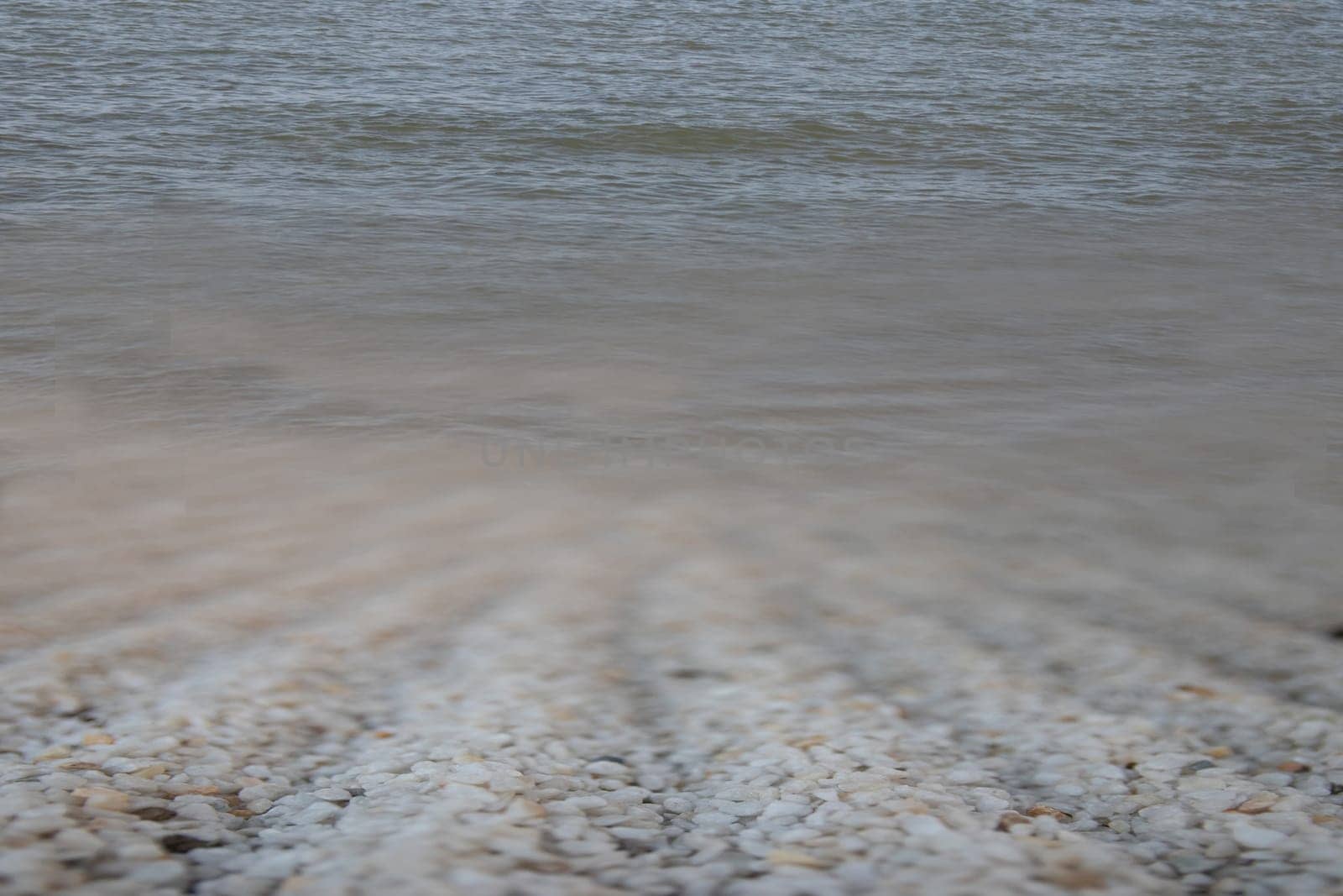 Water background texture with soft waves and white stones in foreground. Space for text.