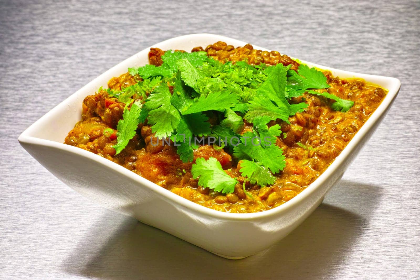 Moong Dahl, indian vegetarian lentil soup, in white bowl. Aluminium background.