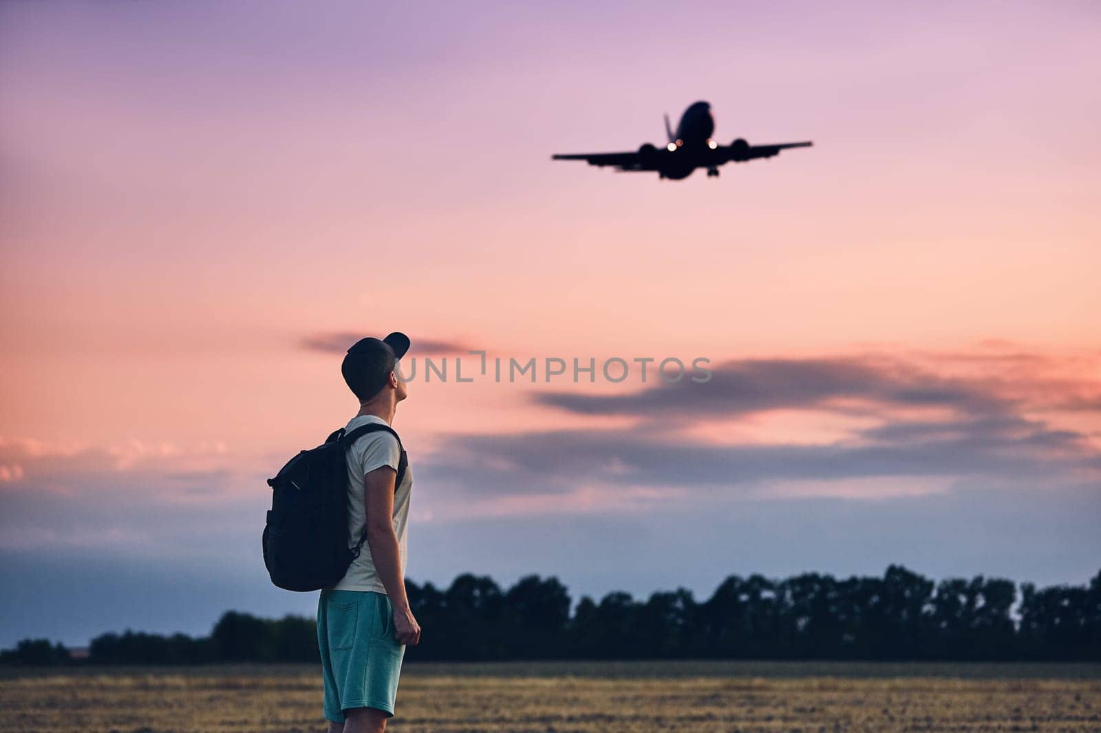 Young man (traveler) against moody sky with landing airplane. Prague, Czech Republic.