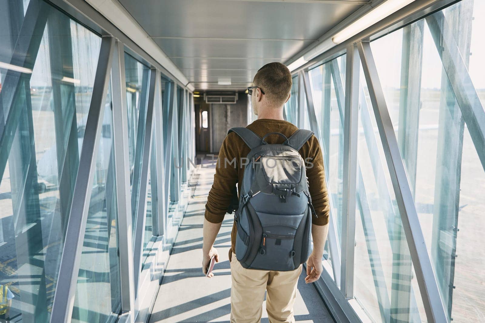 Traveling by airplane. Rear view of young man with backpack and passport in hand during boarding at airport.