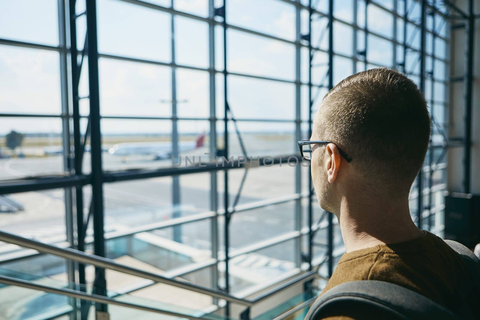 Young passenger waiting at airport and looking through window to airplane.