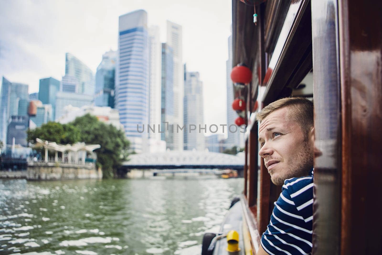 Young man exploring city and looking out from river boat in Singapore.