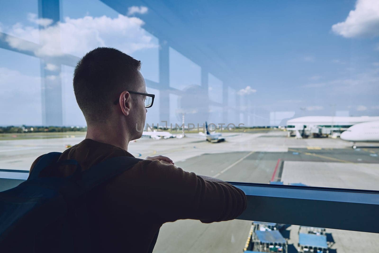 Young passenger waiting at airport and looking through window to airplane.