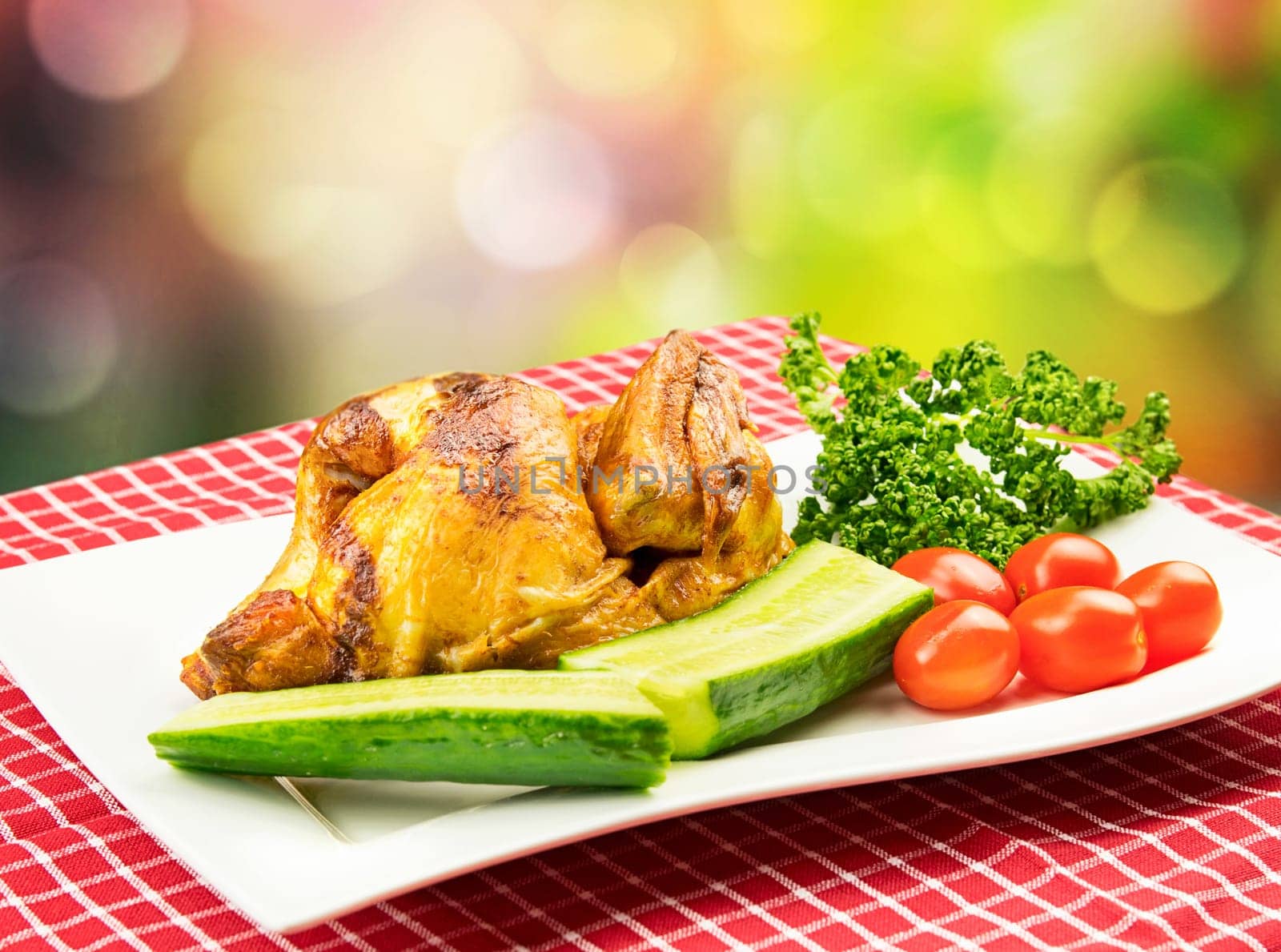 Roasted half chicken with tomatoes, cucumber and parsley on a white plate in BBQ picnic style against bright multicolor background. Concept advertisement.