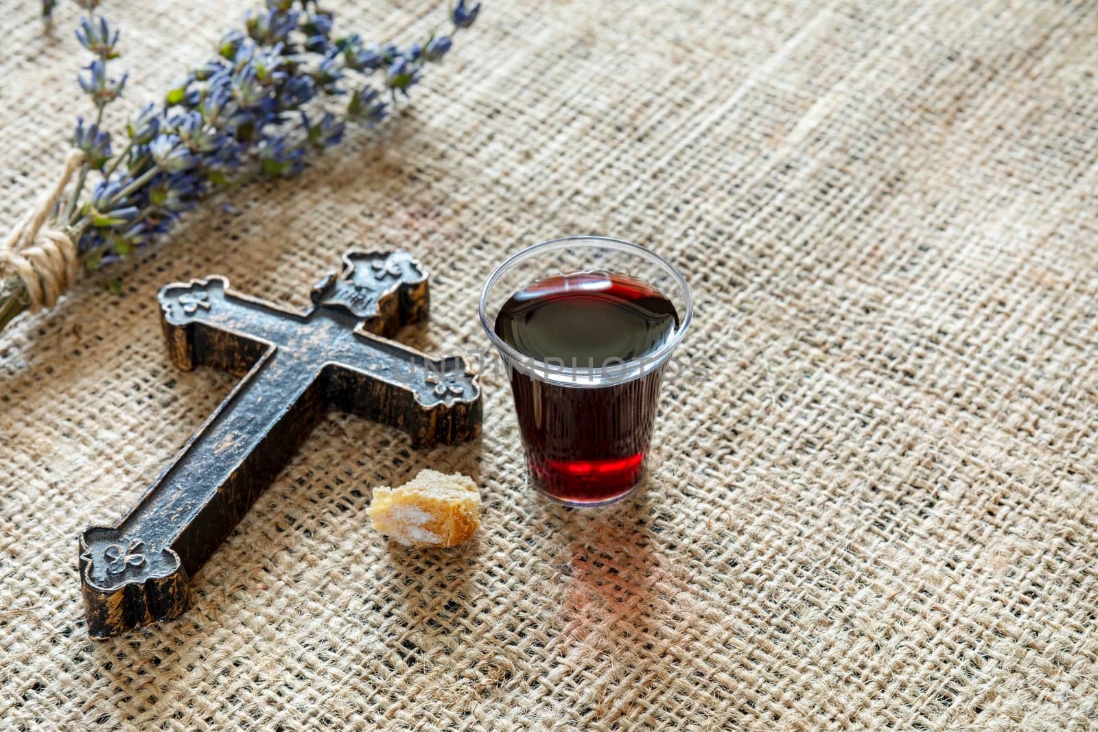 Taking communion with glass of wine and bread near cross and lavanda on the textile tablecloth.