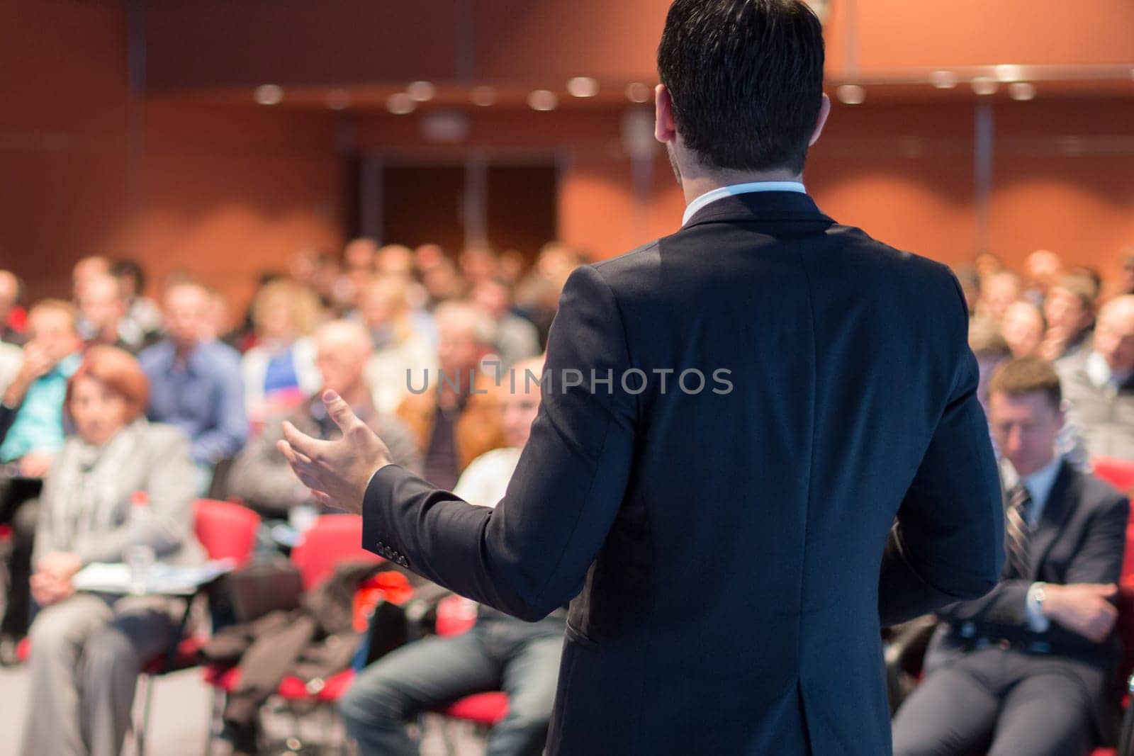 Speaker giving a talk on corporate business conference. Unrecognizable people in audience at conference hall. Business and Entrepreneurship event.