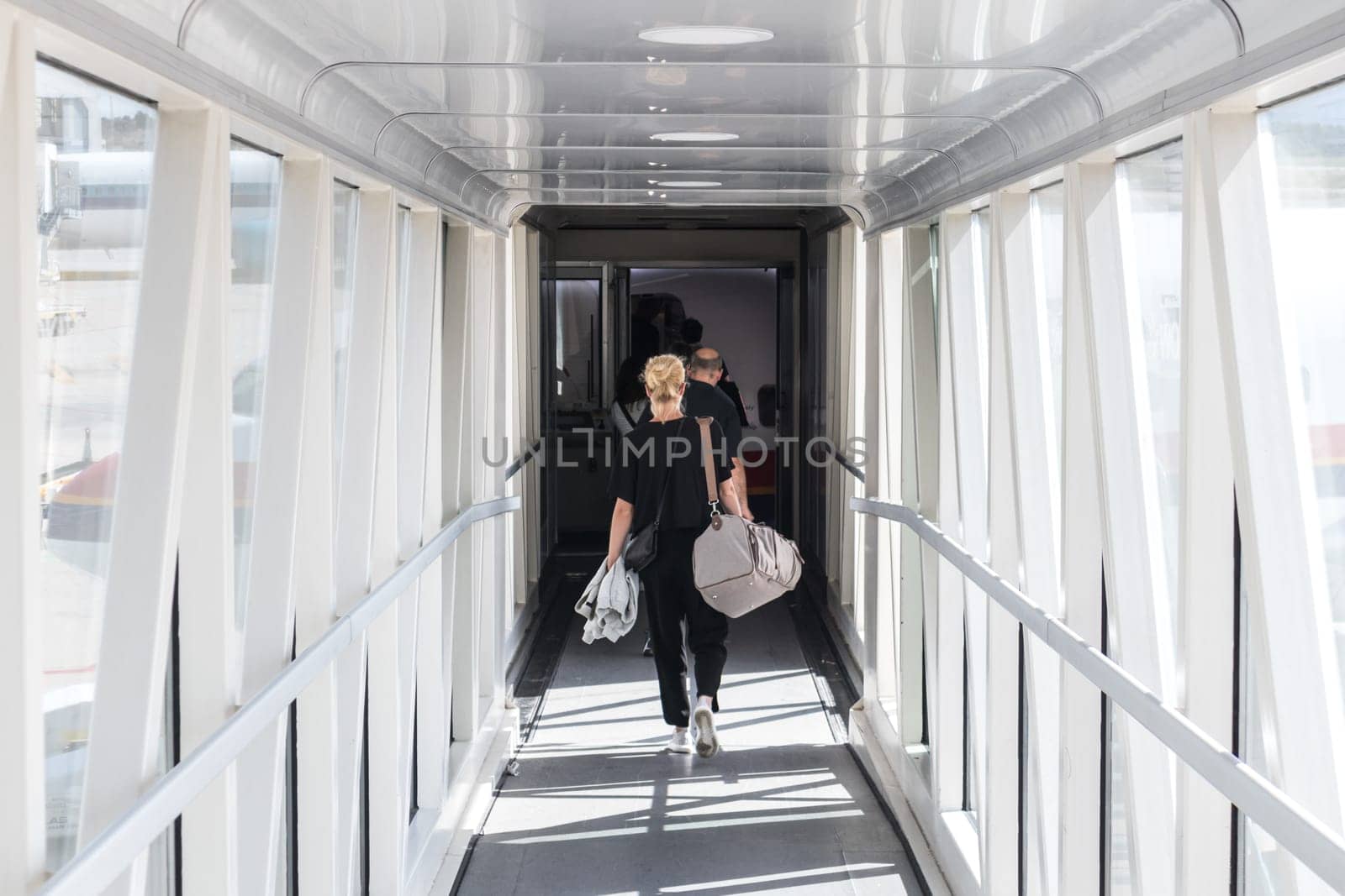 Airplane Boarding. Casual female passenger carrying the hand luggage bag, walking the airplane boarding corridor.