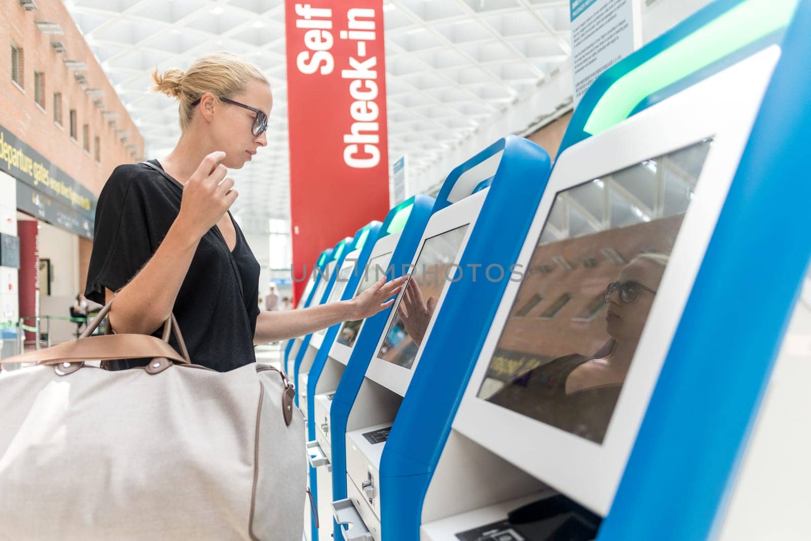 Casual caucasian woman using smart phone application and check-in machine at the airport getting the boarding pass. Modern technology on airport.