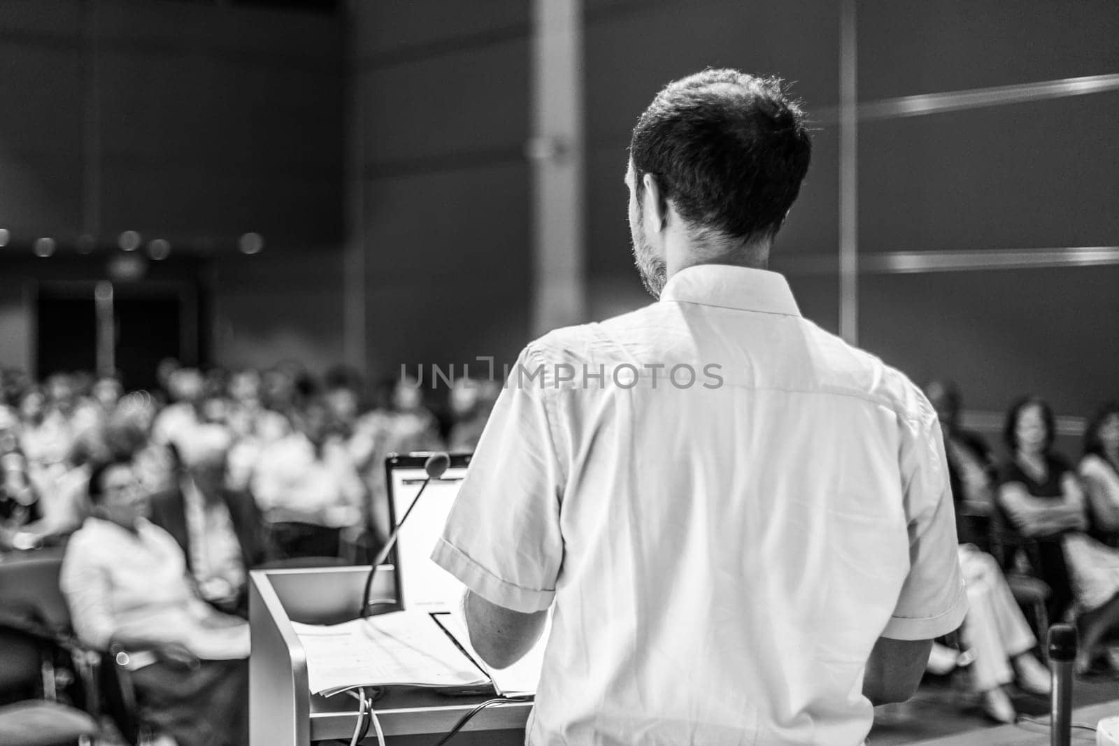Speaker giving a talk on corporate business conference. Unrecognizable people in audience at conference hall. Business and Entrepreneurship event. Black and white image.