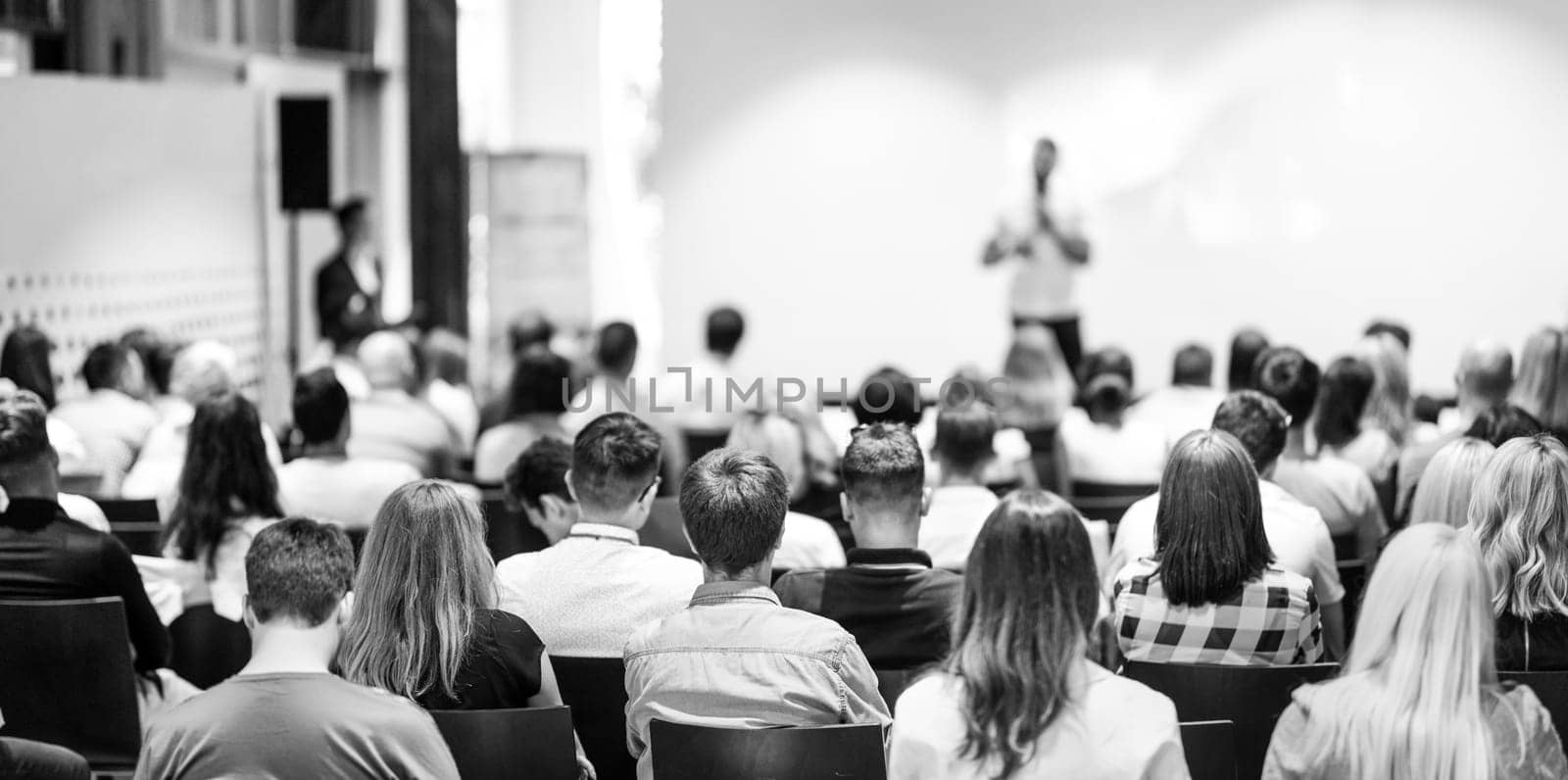 Speaker giving a talk in conference hall at business event. Focus on unrecognizable people in audience. Business and Entrepreneurship concept. Black and white image.