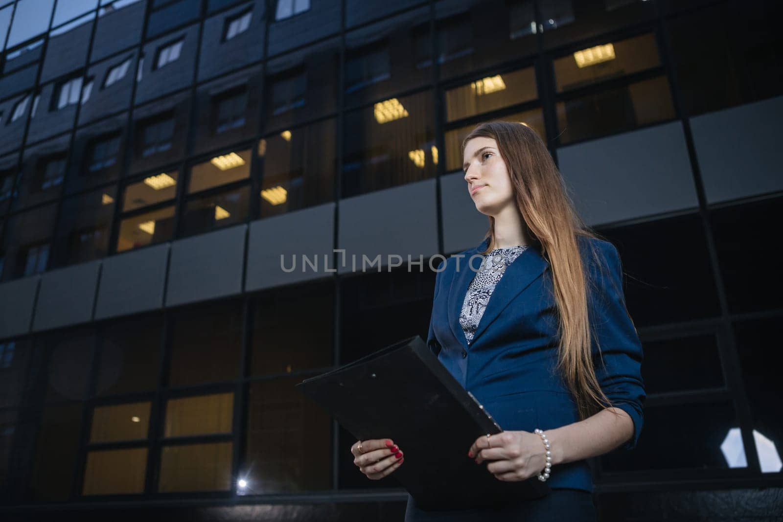 Successful beautiful young business woman standing against a background of buildings and holding folder.